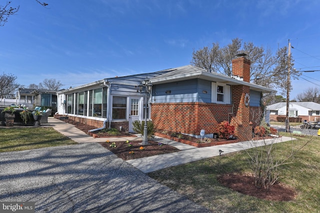 view of side of property featuring brick siding, fence, a chimney, a yard, and a sunroom