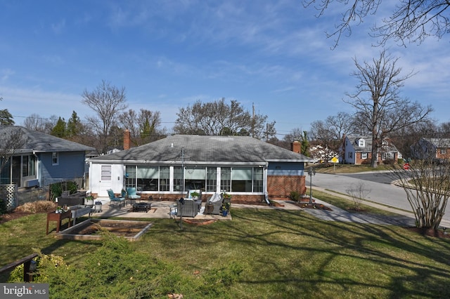 back of property with a yard, brick siding, a chimney, and an outdoor fire pit