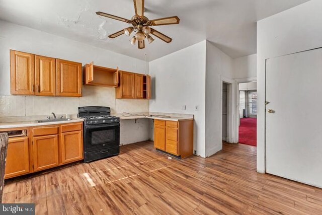 kitchen with light wood finished floors, ceiling fan, a sink, and gas stove