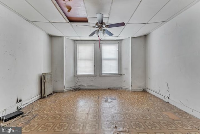 empty room featuring ceiling fan, a drop ceiling, tile patterned floors, and radiator