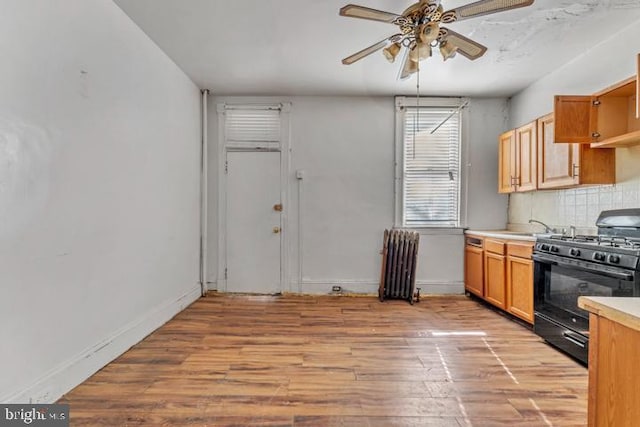 kitchen with black gas range, radiator heating unit, light wood-style flooring, light countertops, and backsplash