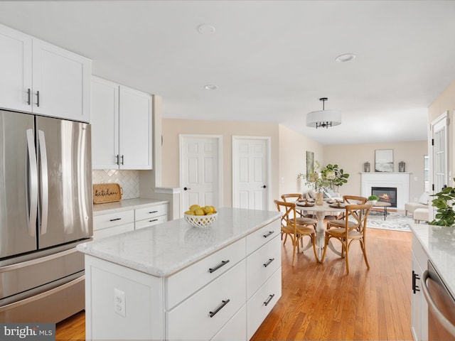 kitchen featuring light wood finished floors, appliances with stainless steel finishes, white cabinets, and tasteful backsplash