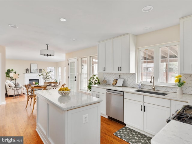 kitchen with decorative backsplash, a glass covered fireplace, a center island, stainless steel dishwasher, and a sink