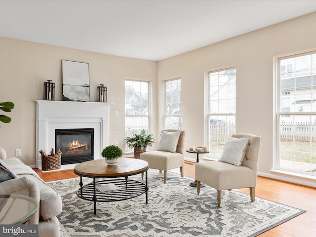 living area with a wealth of natural light, a glass covered fireplace, and wood finished floors