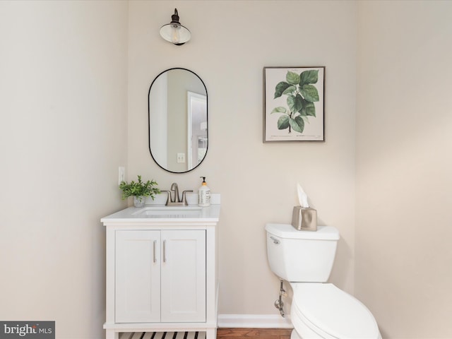 half bath featuring baseboards, vanity, and toilet