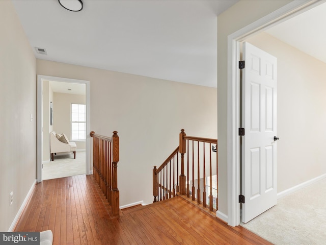 hall with wood-type flooring, visible vents, baseboards, and an upstairs landing