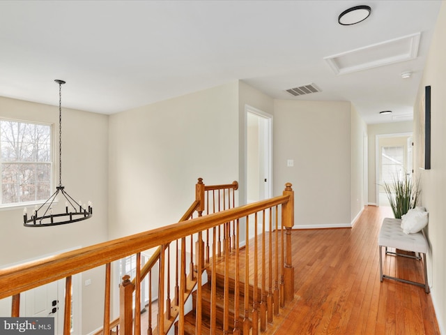 hallway featuring wood-type flooring, visible vents, attic access, an upstairs landing, and baseboards