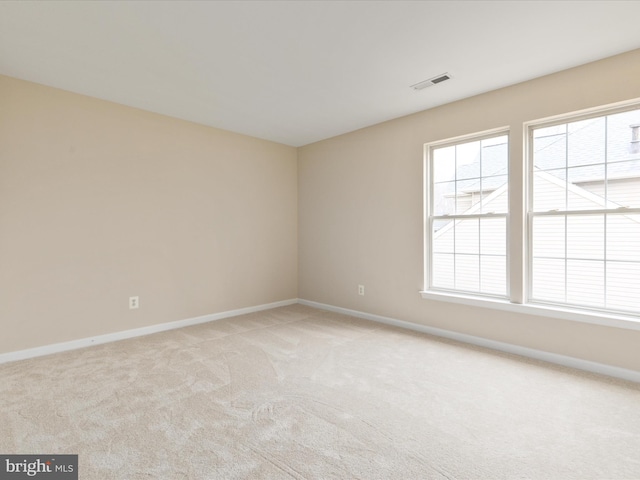 empty room with baseboards, visible vents, and light colored carpet