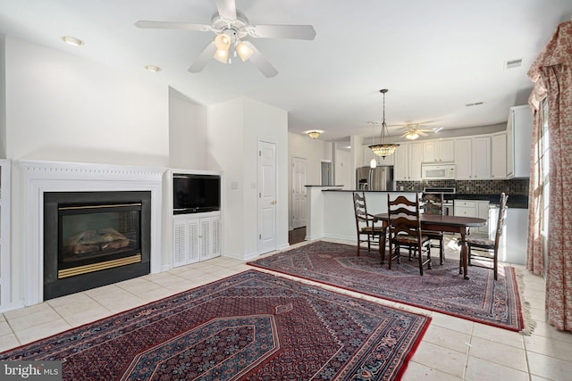 dining area with light tile patterned floors, visible vents, a ceiling fan, a glass covered fireplace, and baseboards