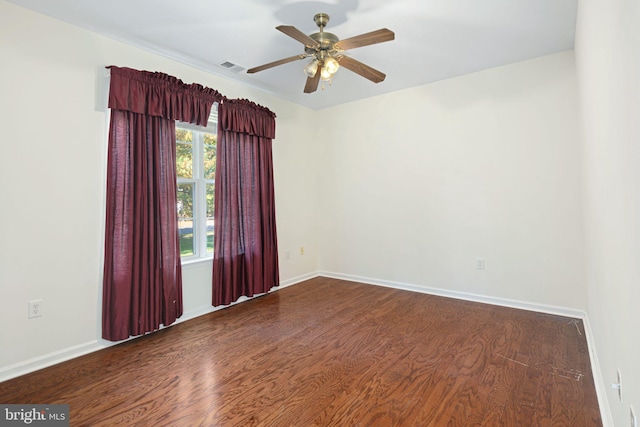 empty room featuring a ceiling fan, baseboards, visible vents, and dark wood-type flooring