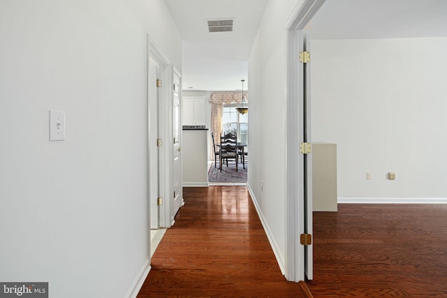 hallway featuring dark wood finished floors, visible vents, and baseboards