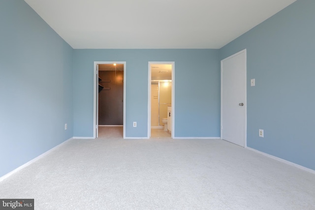 unfurnished bedroom with connected bathroom, light colored carpet, baseboards, a closet, and a walk in closet