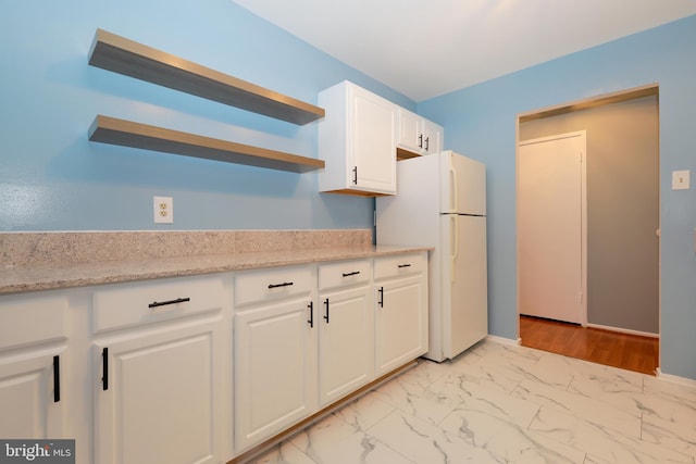 kitchen featuring marble finish floor, open shelves, freestanding refrigerator, white cabinets, and light stone countertops