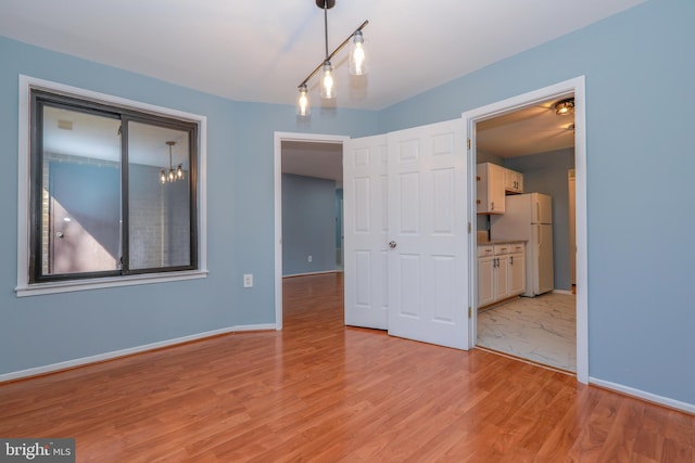 unfurnished bedroom featuring light wood-type flooring, connected bathroom, freestanding refrigerator, and baseboards