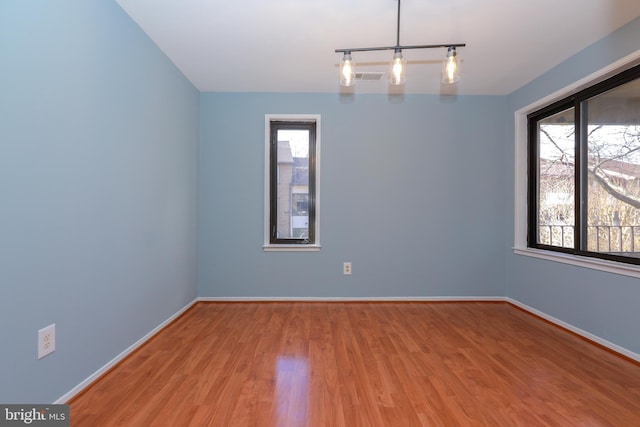 unfurnished room with rail lighting, visible vents, baseboards, and wood finished floors