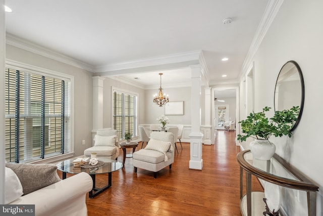 living area featuring crown molding, a notable chandelier, recessed lighting, wood finished floors, and ornate columns