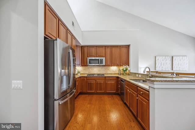 kitchen with light stone counters, brown cabinets, stainless steel appliances, tasteful backsplash, and a sink