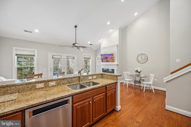 kitchen with a sink, visible vents, light wood-style floors, dishwasher, and a glass covered fireplace