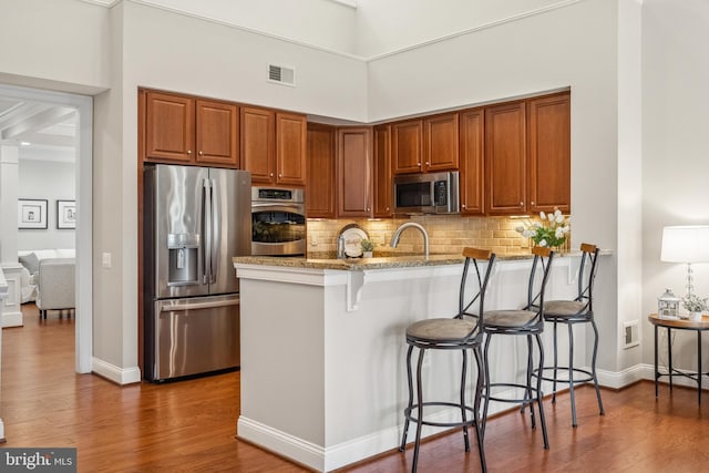 kitchen featuring backsplash, appliances with stainless steel finishes, wood finished floors, a peninsula, and a kitchen breakfast bar