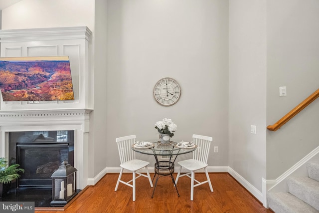 dining room with a glass covered fireplace, wood finished floors, baseboards, and stairs