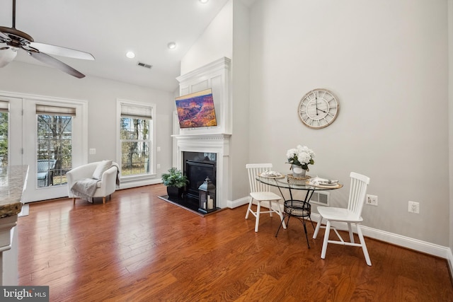 interior space with baseboards, visible vents, a glass covered fireplace, wood finished floors, and high vaulted ceiling