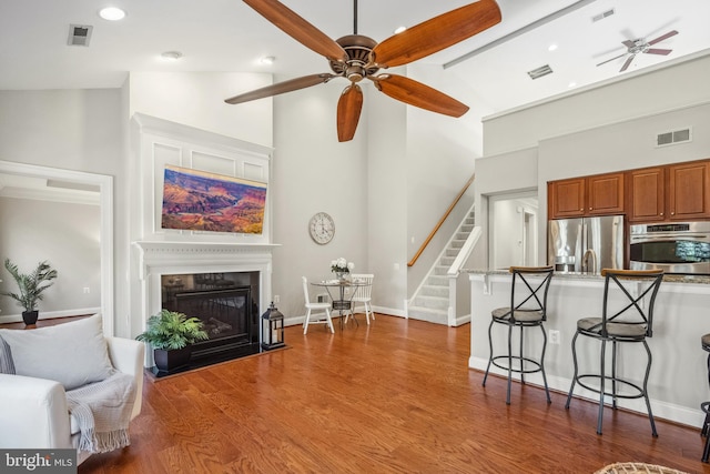 living area featuring ceiling fan, wood finished floors, visible vents, stairs, and a glass covered fireplace