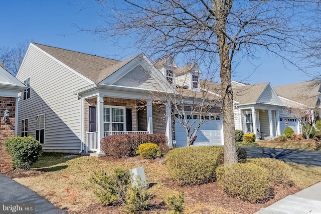 view of front of house featuring brick siding, roof with shingles, covered porch, a garage, and driveway