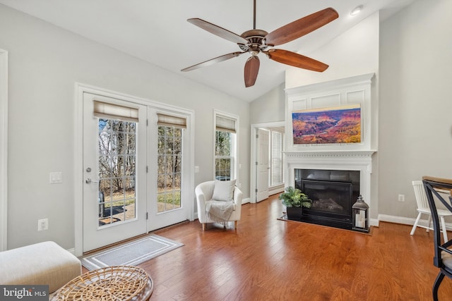 living area with a fireplace with flush hearth, a ceiling fan, vaulted ceiling, wood finished floors, and baseboards