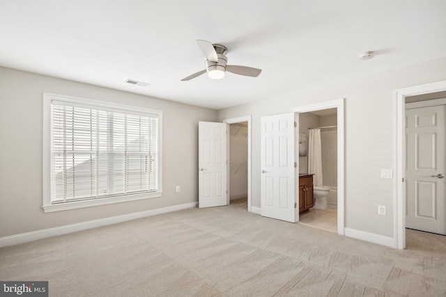 unfurnished bedroom featuring visible vents, a spacious closet, light carpet, ensuite bath, and baseboards