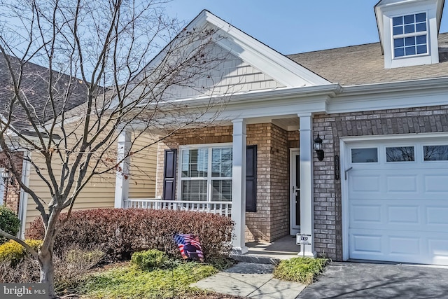 doorway to property featuring an attached garage, covered porch, roof with shingles, and brick siding