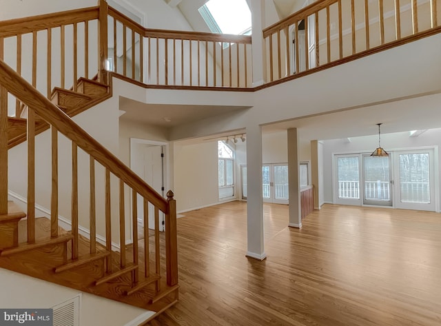 stairs with a skylight, a high ceiling, baseboards, and wood finished floors