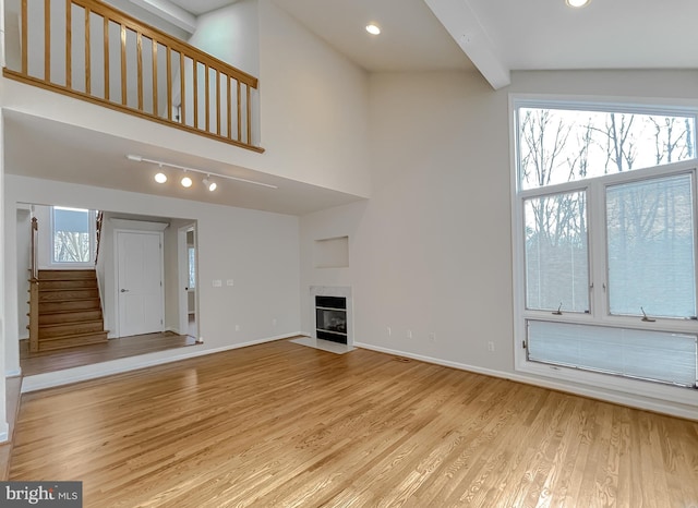 unfurnished living room featuring beam ceiling, a fireplace with flush hearth, wood finished floors, baseboards, and stairs