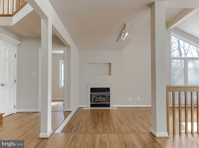 unfurnished living room featuring rail lighting, wood finished floors, a high end fireplace, and baseboards