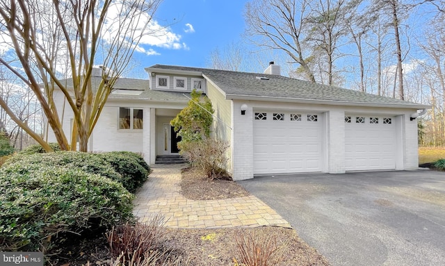 view of front of property with a shingled roof, a chimney, a detached garage, and brick siding