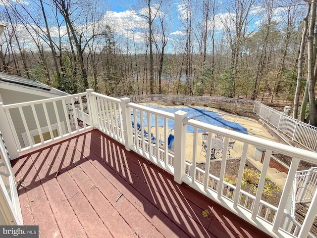 wooden deck featuring a forest view, fence, and a community pool