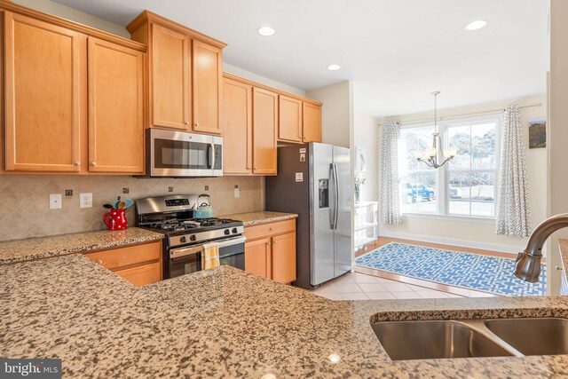 kitchen with light stone counters, a sink, decorative backsplash, stainless steel appliances, and a chandelier