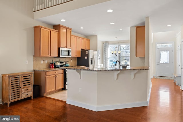 kitchen featuring light wood finished floors, a peninsula, stone countertops, stainless steel appliances, and a kitchen bar