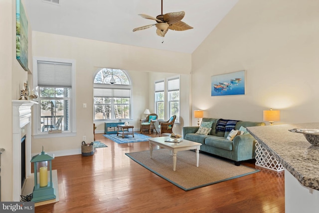 living room featuring a ceiling fan, visible vents, wood finished floors, baseboards, and high vaulted ceiling