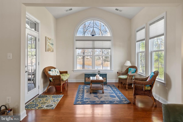 living area with visible vents, lofted ceiling, baseboards, and wood finished floors