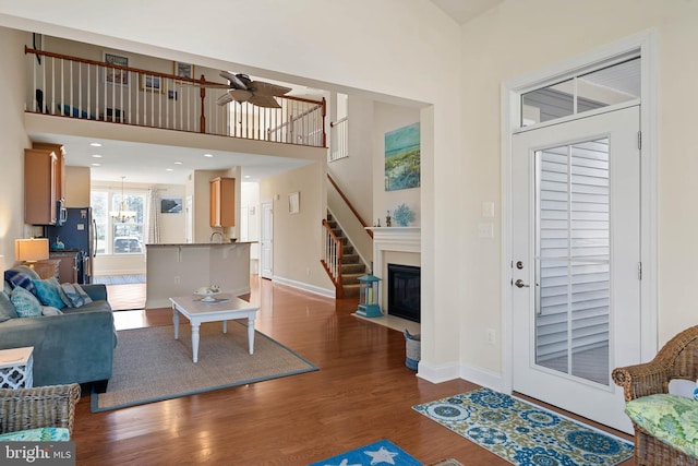 living room with ceiling fan, baseboards, wood finished floors, and a towering ceiling