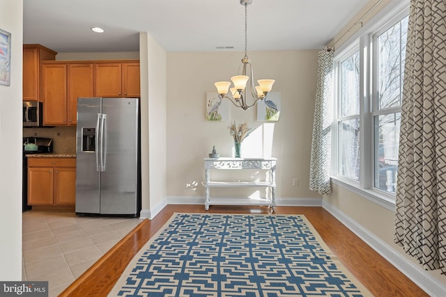 kitchen with a wealth of natural light, a notable chandelier, light wood finished floors, and appliances with stainless steel finishes