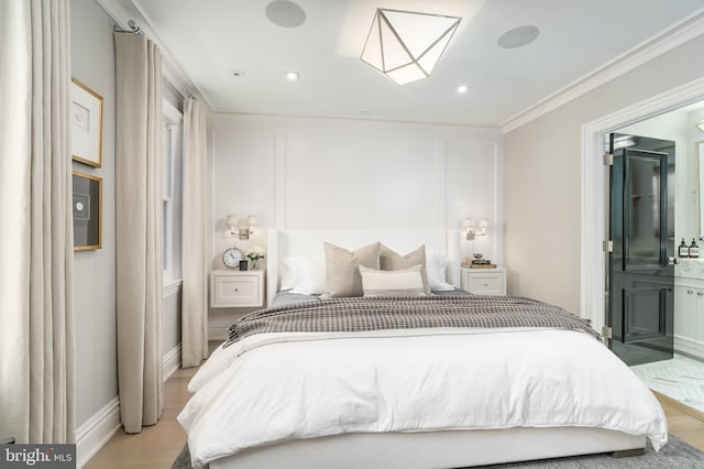 bedroom featuring light wood-style floors, a decorative wall, ensuite bath, and crown molding