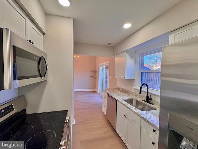 kitchen with appliances with stainless steel finishes, white cabinets, a sink, and light stone countertops