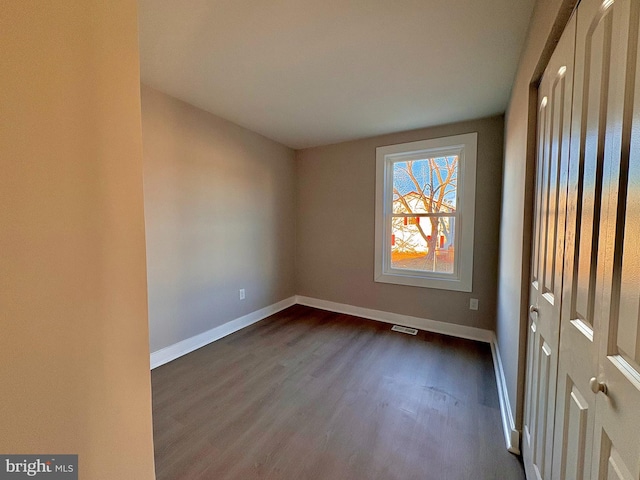 unfurnished room with baseboards and dark wood-type flooring