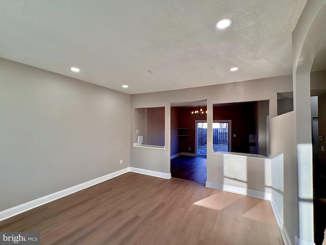 empty room featuring baseboards, wood finished floors, an inviting chandelier, a textured ceiling, and recessed lighting