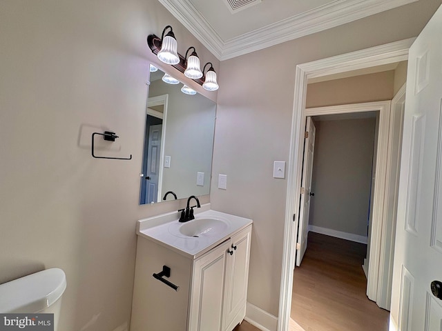 half bathroom with crown molding, toilet, vanity, wood finished floors, and baseboards