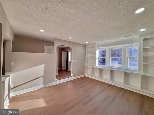 unfurnished room featuring a textured ceiling, arched walkways, wood finished floors, and recessed lighting