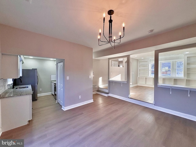 unfurnished dining area with baseboards, visible vents, a chandelier, and wood finished floors