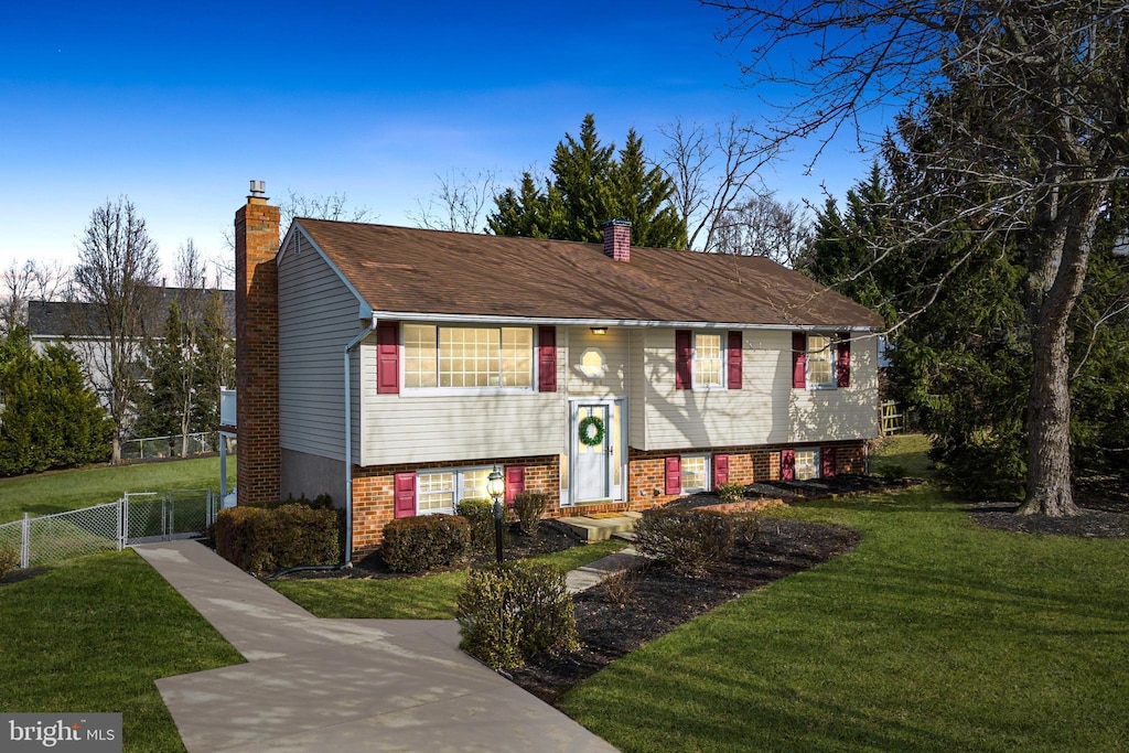 raised ranch with a front lawn, a chimney, and fence