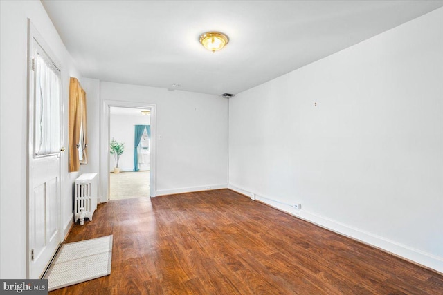 empty room with baseboards, visible vents, radiator heating unit, and wood finished floors